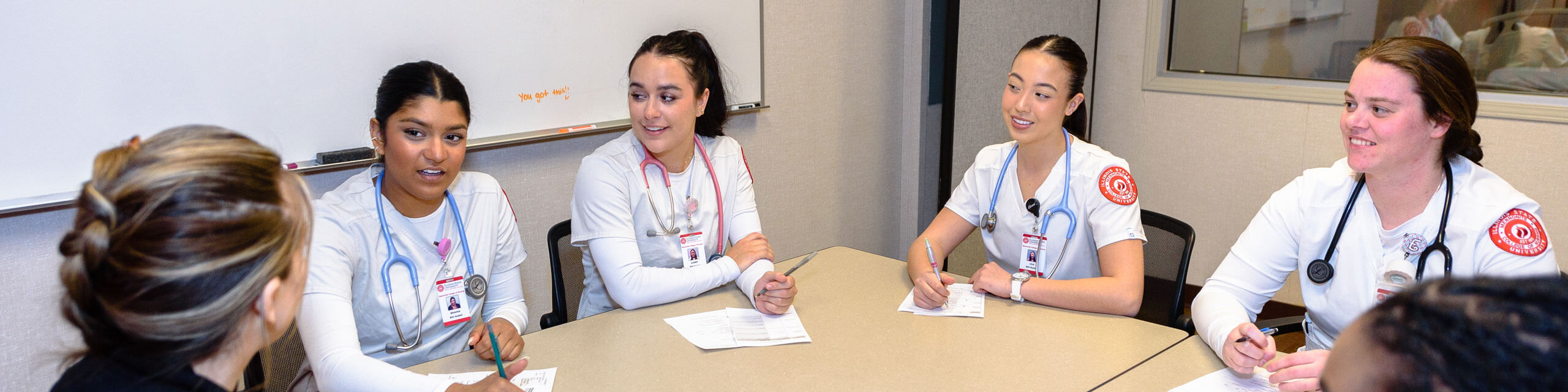 Student nurses meet at a table with their instructor.