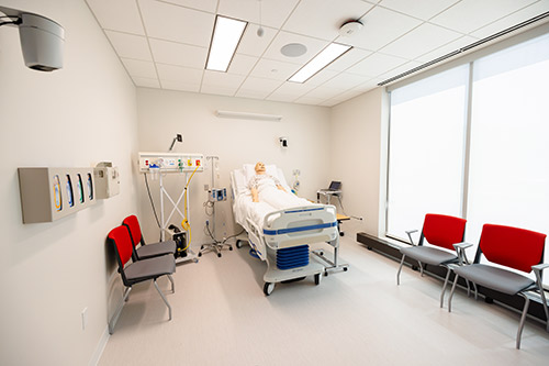 A simulation of a hospital room with a bed, medical equipment, and two chairs