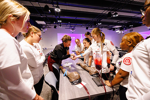 A group of students surrounding a table, focused on a mannequin positioned prominently in their midst.