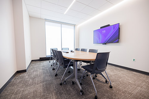 A modern conference room featuring a large flat screen TV mounted on the wall, surrounded by a sleek table and chairs.